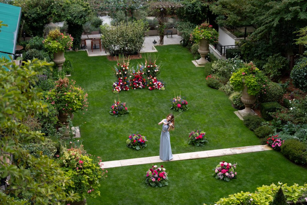 A secluded garden at the Shangri-La Paris awaits a couple’s luxury proposal. A violinist serenades amidst vibrant flowers, creating a private ambiance.