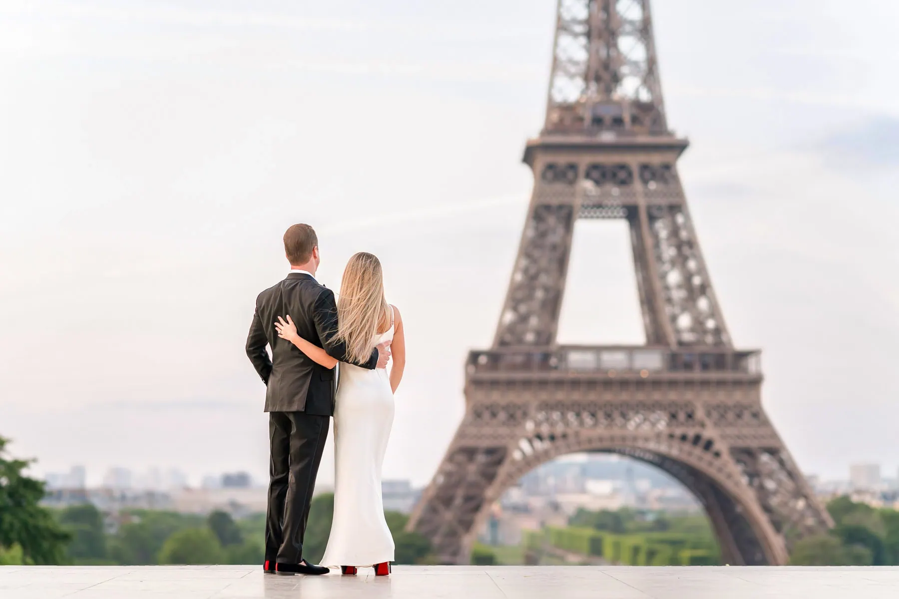 Stylish couple in Louboutins embracing during sunrise Paris engagement photo shoot at Trocadero with Eiffel Tower view