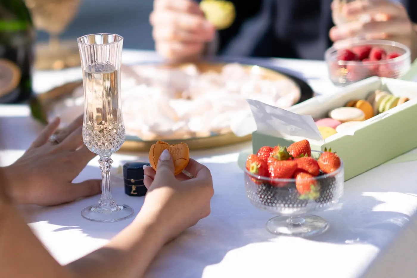 Couple enjoying a luxury Paris picnic proposal by the Seine River with personalized LaDuree macarons, champagne, and fresh fruit